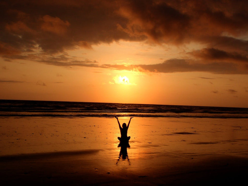 A person practicing yoga on the beach at sunset, symbolizing tranquility and wellness.
